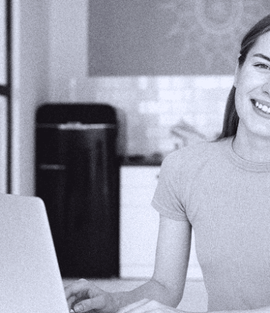 foto-em-preto-e-branco-com-detalhes-azuis-de-mulher-sorrindo-diante-de-sua-mesa-de-trabalho