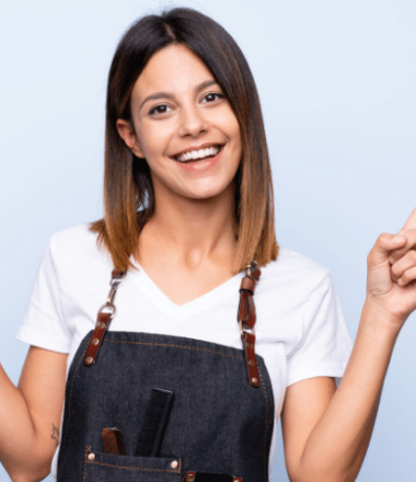 foto-de-mulher-segurando-ferramentas-de-trabalho-de-cabeleireira-com-um-avental-e-parede-azul-para-ilustrar-o-mercado-de-saloes-de-beleza